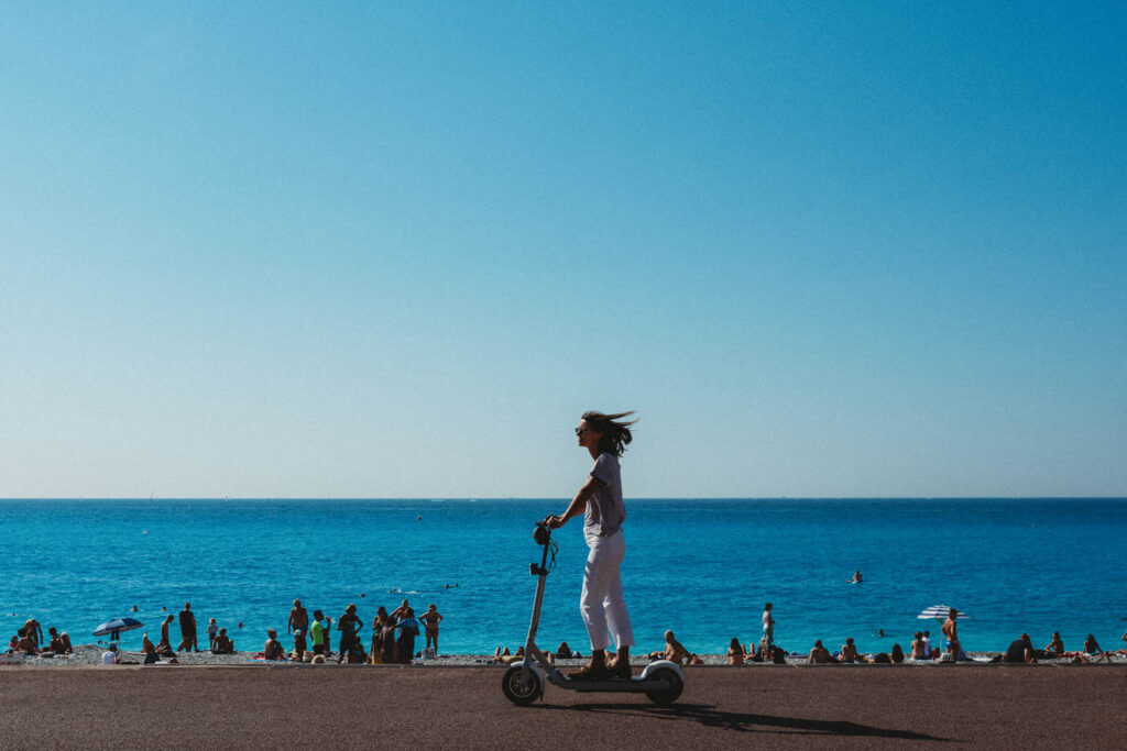 Girl on a scooter on the promenade with view of the beach and sea in Nice