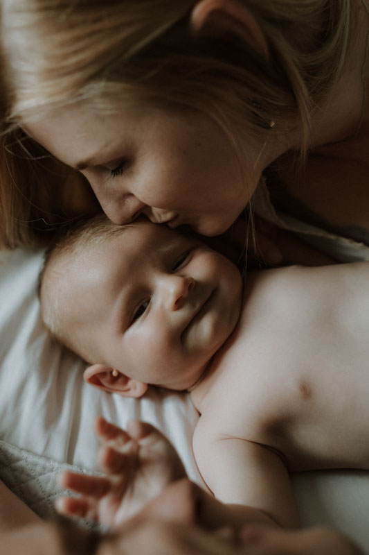 Bébé fait un petit sourire pendant que sa mère l’embrasse.